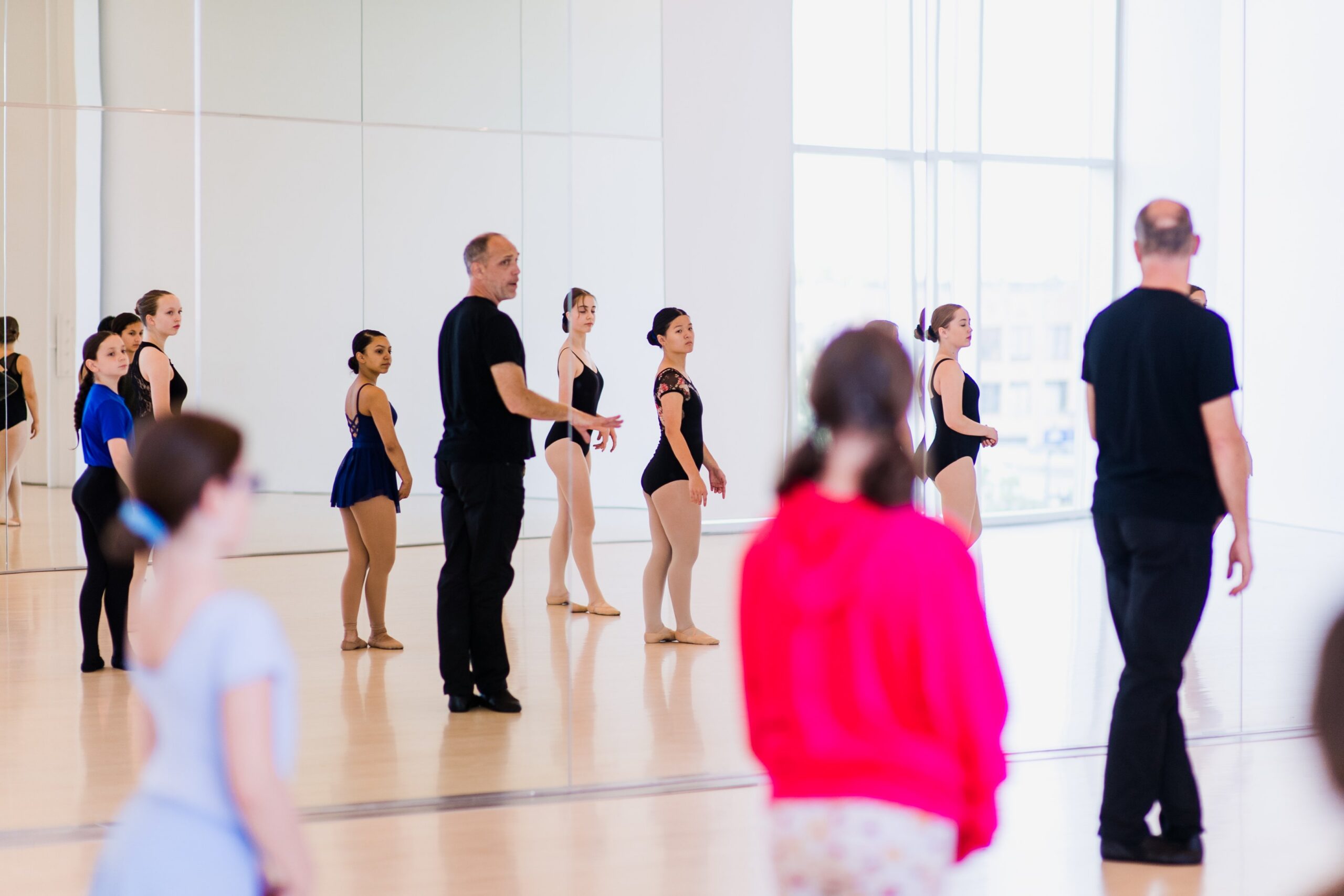 Dancers in leotards stand in a mirrored room