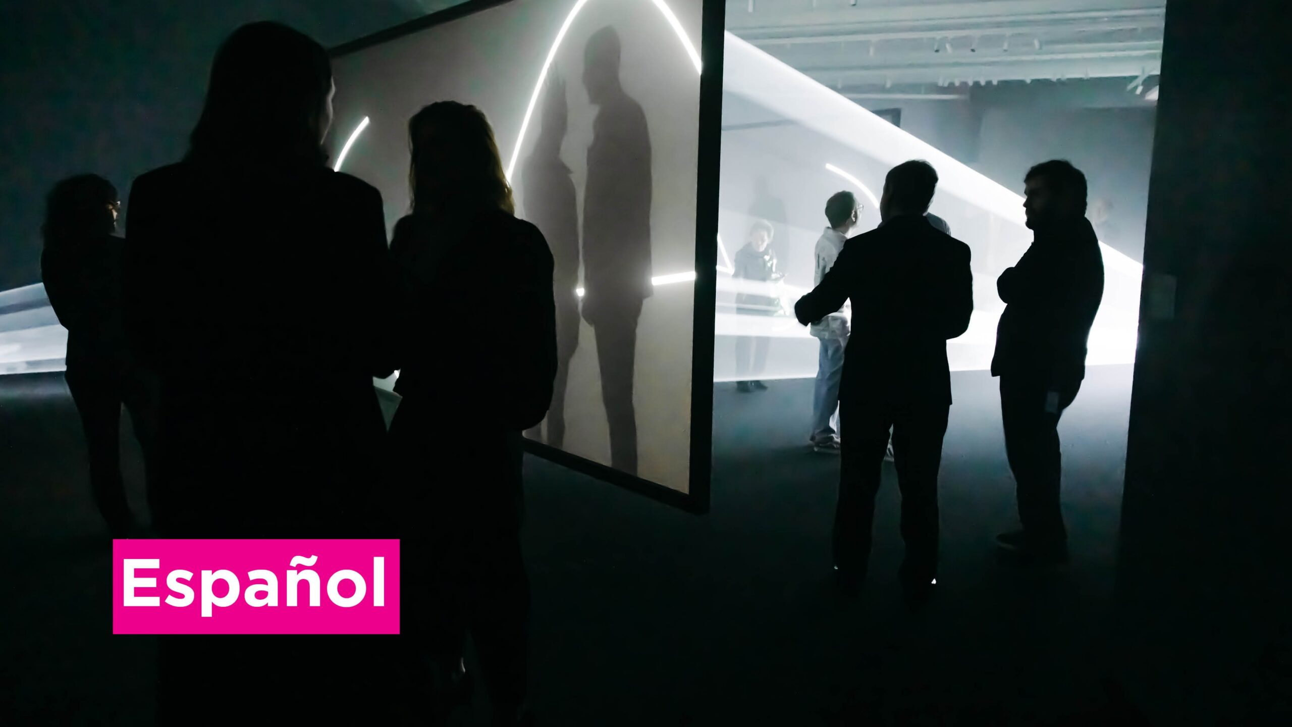 People stand in a dark gallery full of light sculptures