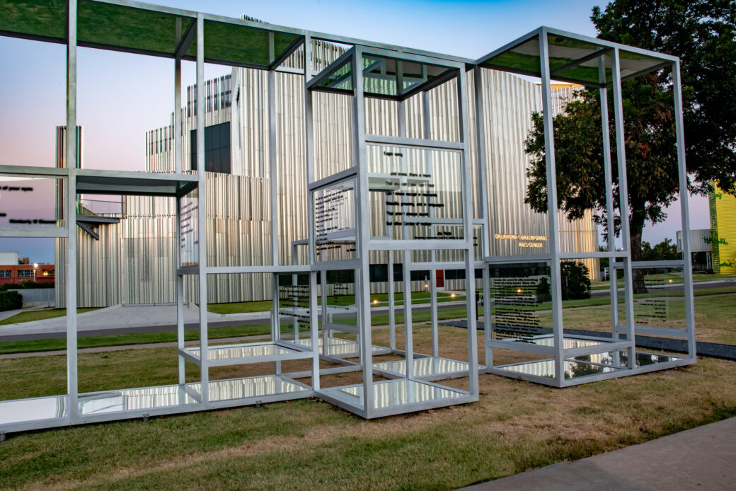 A glass and metal structure in front of a silver building