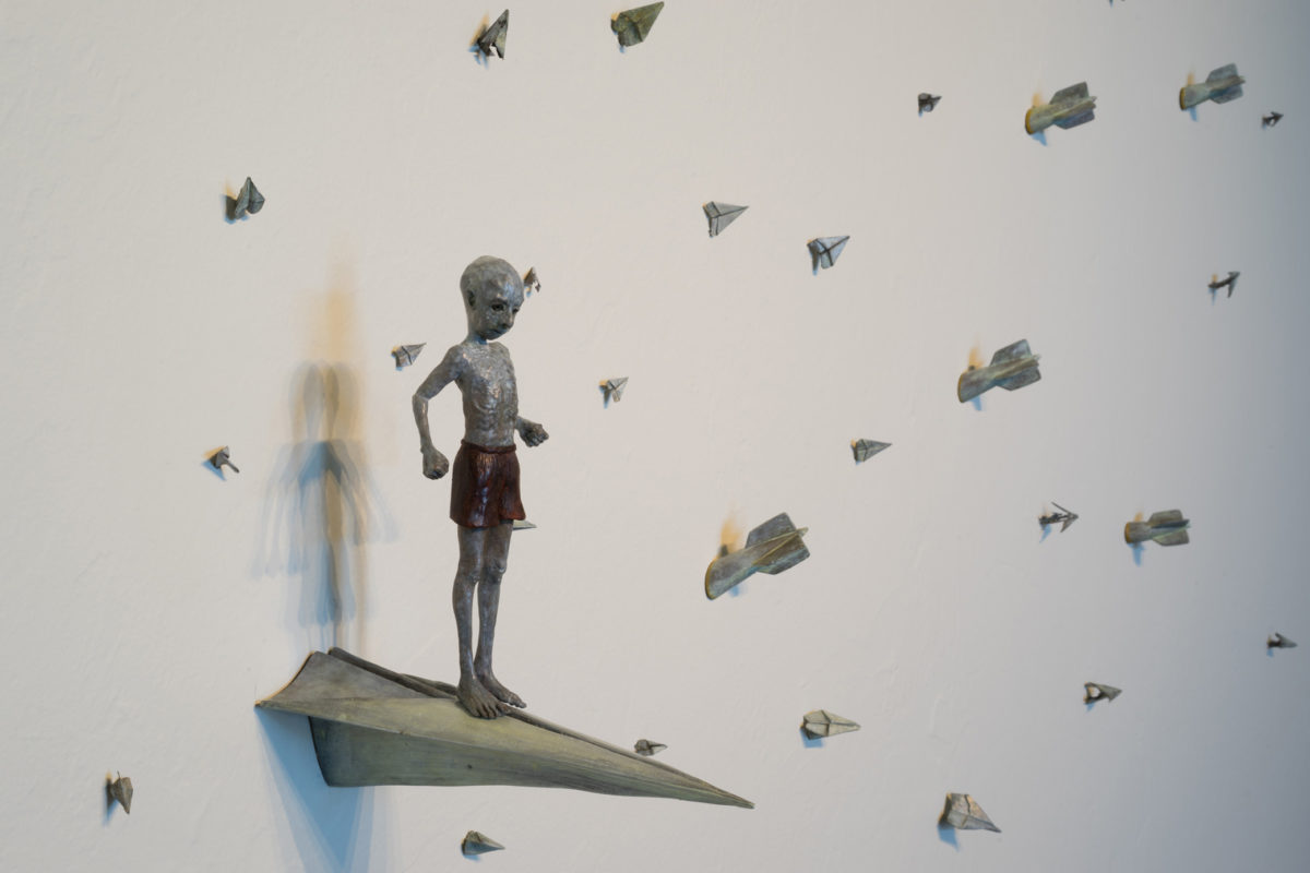 A small figurine standing on a replica of paper airplane while other planes dot the wall around him