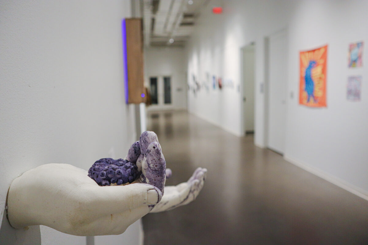 A hallway filled with artwork. The closest object is a white sculpture of a hand holding a purple object.