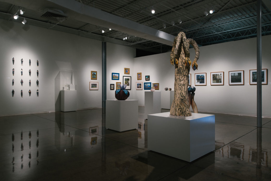 A white gallery filled with various sculptures and wall hangings