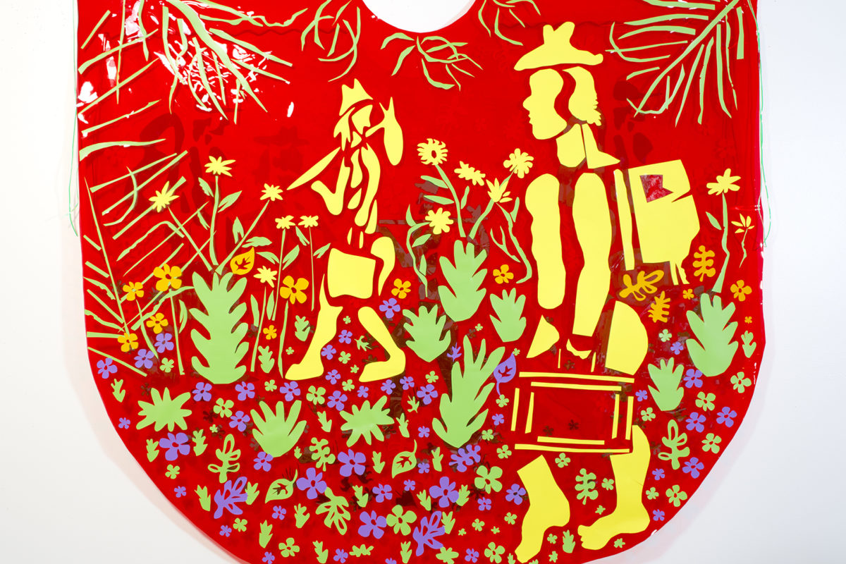 A 2-D mixed-media sculpture features a red background with woodcut-style images of yellow figures walking amid flowers and plants