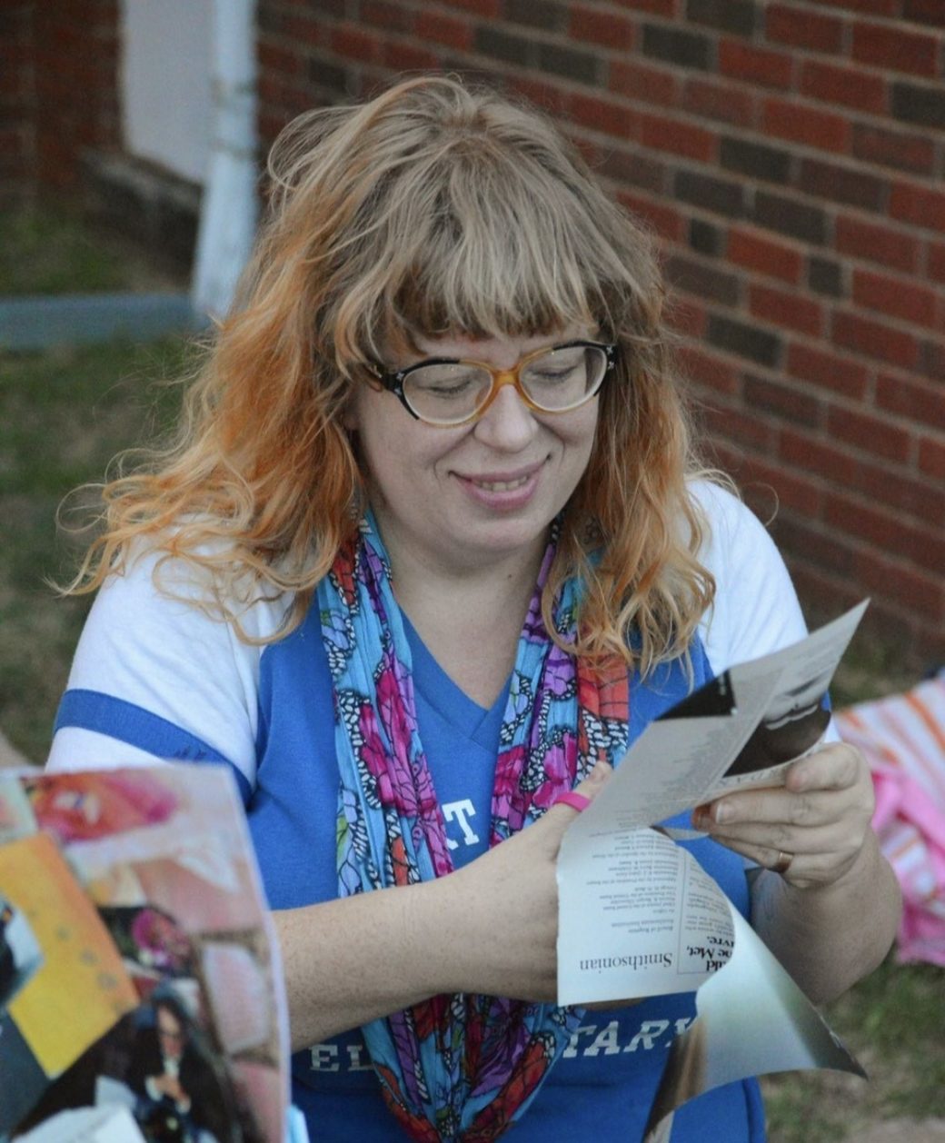 Woman with strawberry blonde hair and glasses focuses on her project of cutting paper