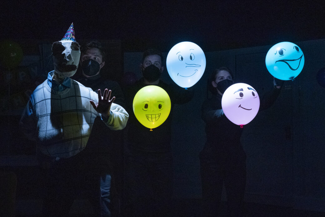 A life-size puppet next to four colorful balloons with faces drawn on