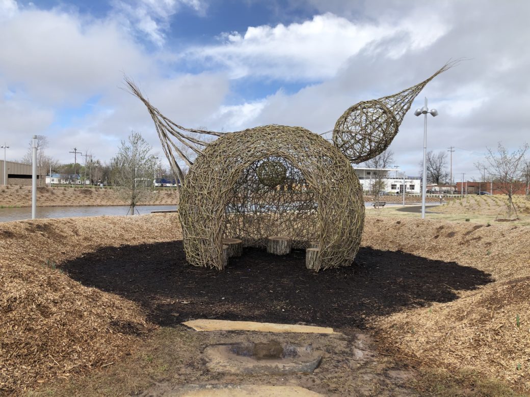 A large bird woven from sticks sits in a park