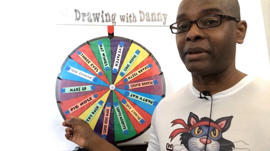 A person wearing glasses and a cartoon character T-shirt points to a colorful spinning wheel