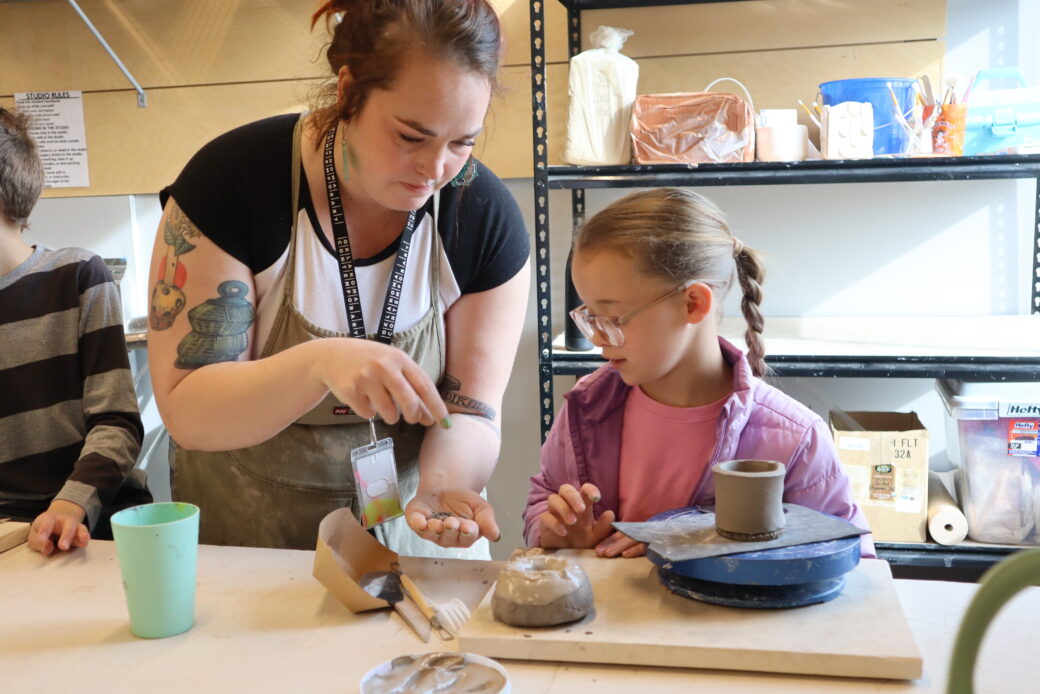 An instructor helps a child with a pottery project