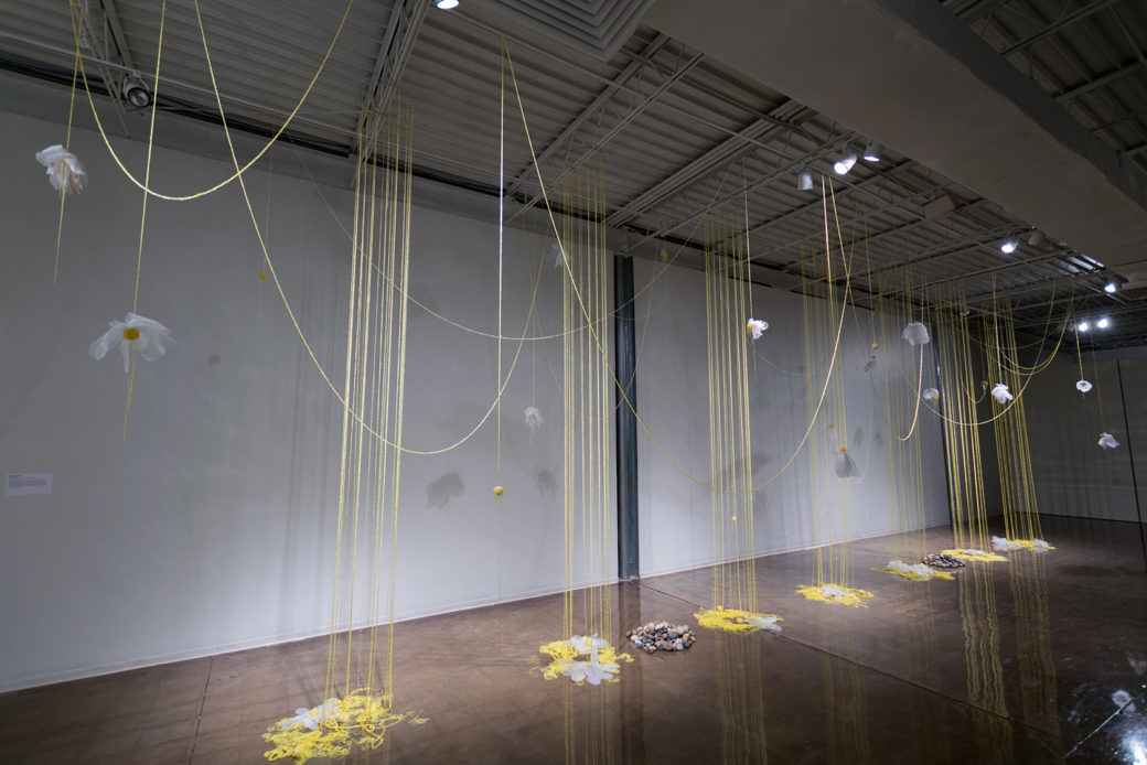 Yellow strings suspend down and across a room with flowers arranged above and to the ground
