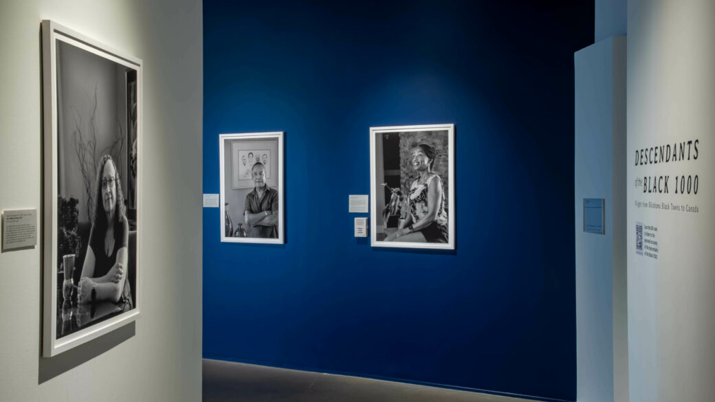 Black-and-white photographic portraits hang on white and blue walls