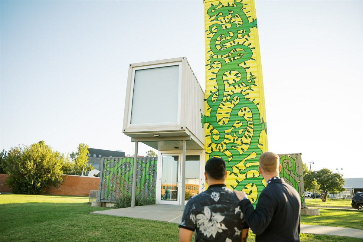 Two people look at a gray and yellow container building painted with green vines