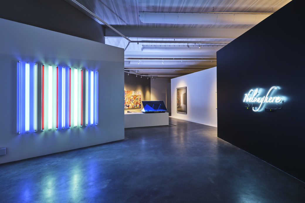 The interior of a contemporary art gallery, featuring vivid light sculptures in the foreground