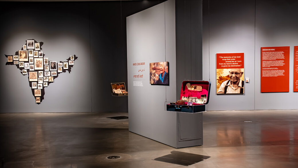 A gallery with suitcases seemingly floating in midair, an outline of India covered in photographs, enlarged photographs, and text printed on large red signs