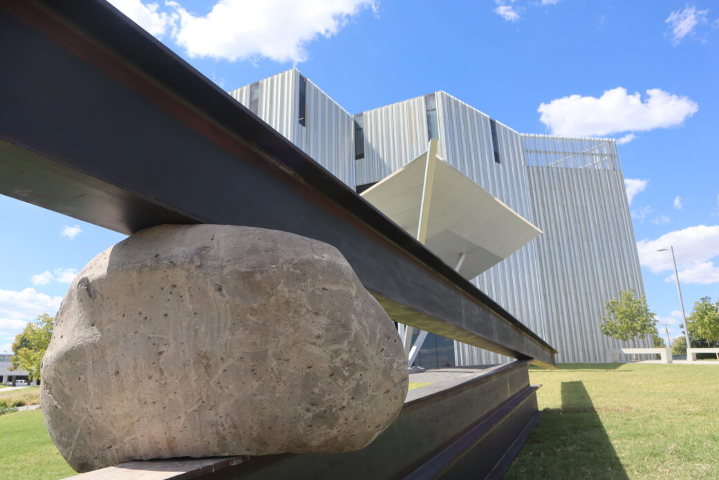 Steel beams and a boulder with a silver building in a background