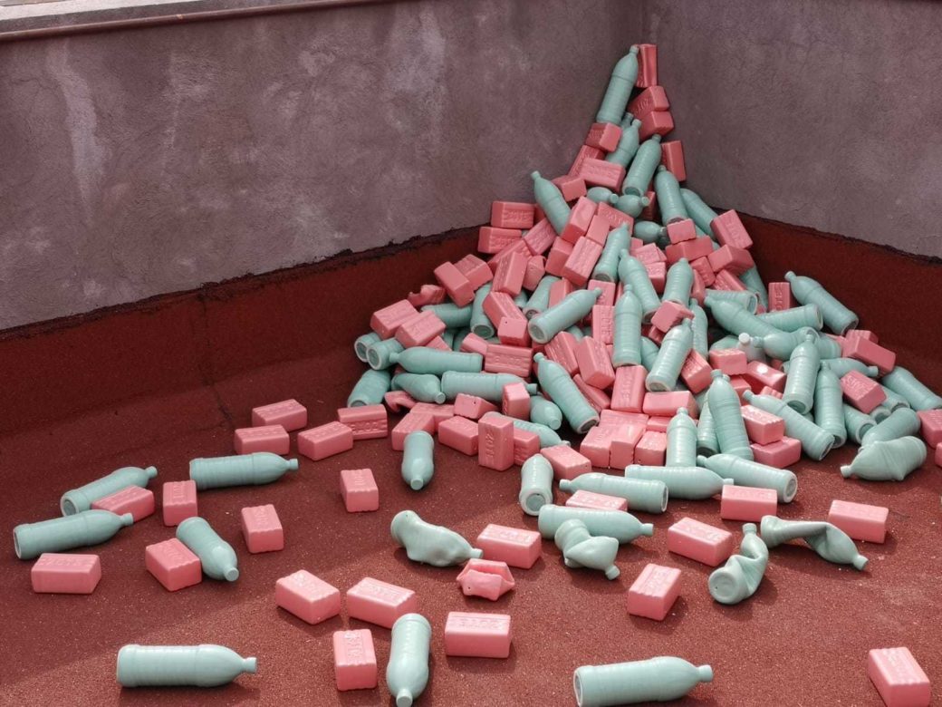 Light blue ceramic bottle and pink ceramic bricks piled in a corner