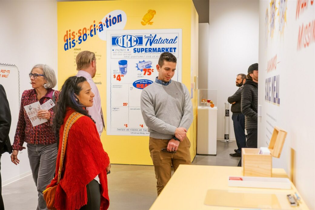 People stand next to a podium. A yellow wall behind them shows a supermarket ad and the title "Dissociation."