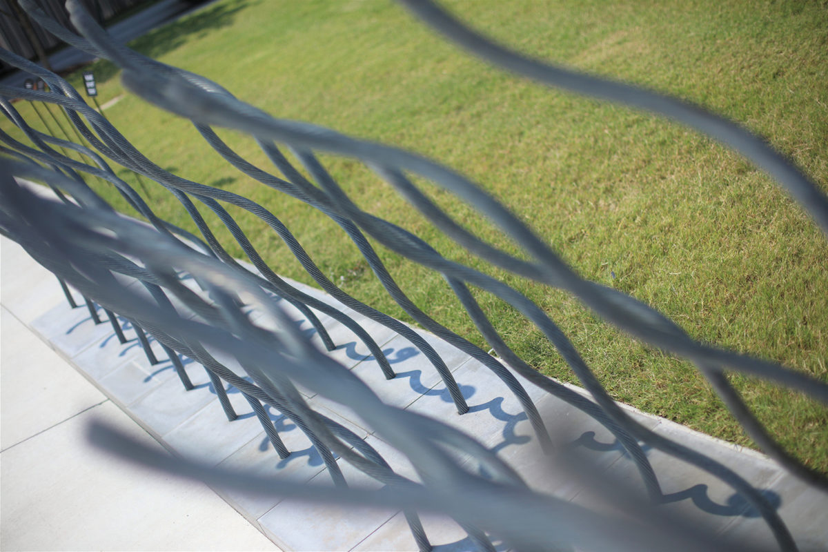 A sculpture of twisted wires rising out of pavers sits between a sidewalk and a lawn