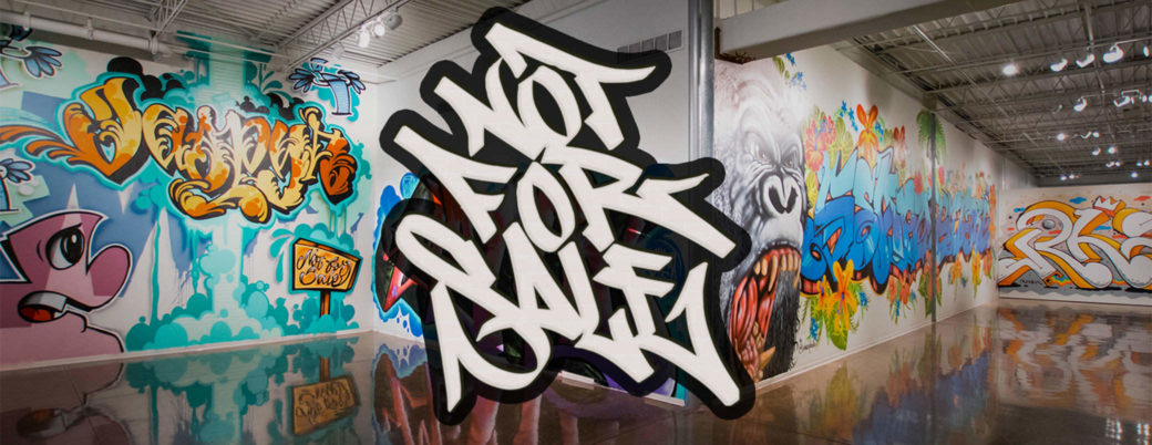 White gallery walls covered in brightly colored graffiti with “Not For Sale” logo overlayed