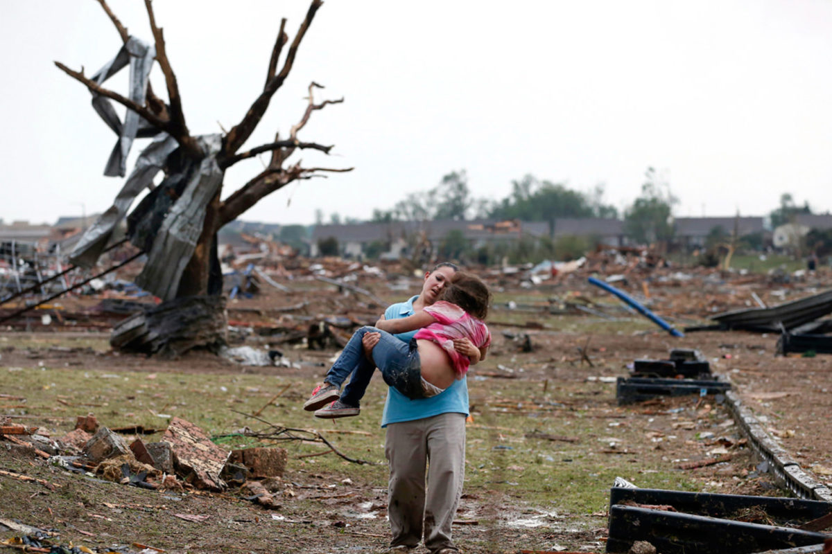 An adult carries a child away from the ruins of a neighborhood
