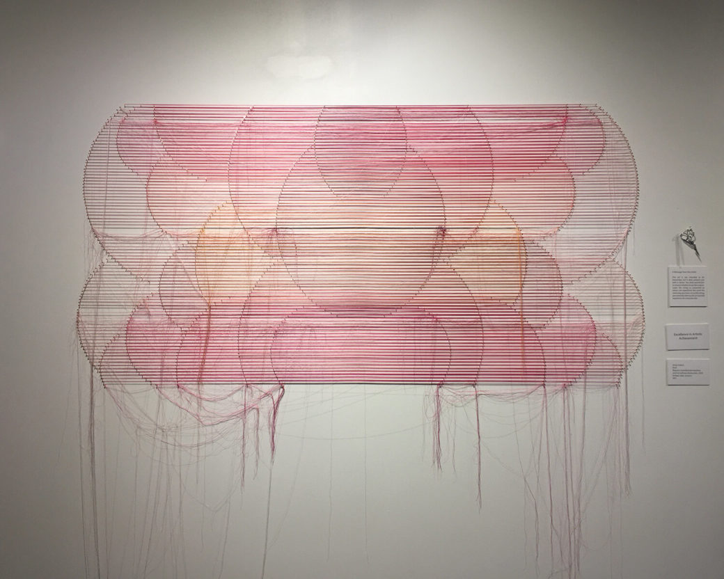 A wall sculpture made of sunset-colored threads in multiple circles hangs on a wall