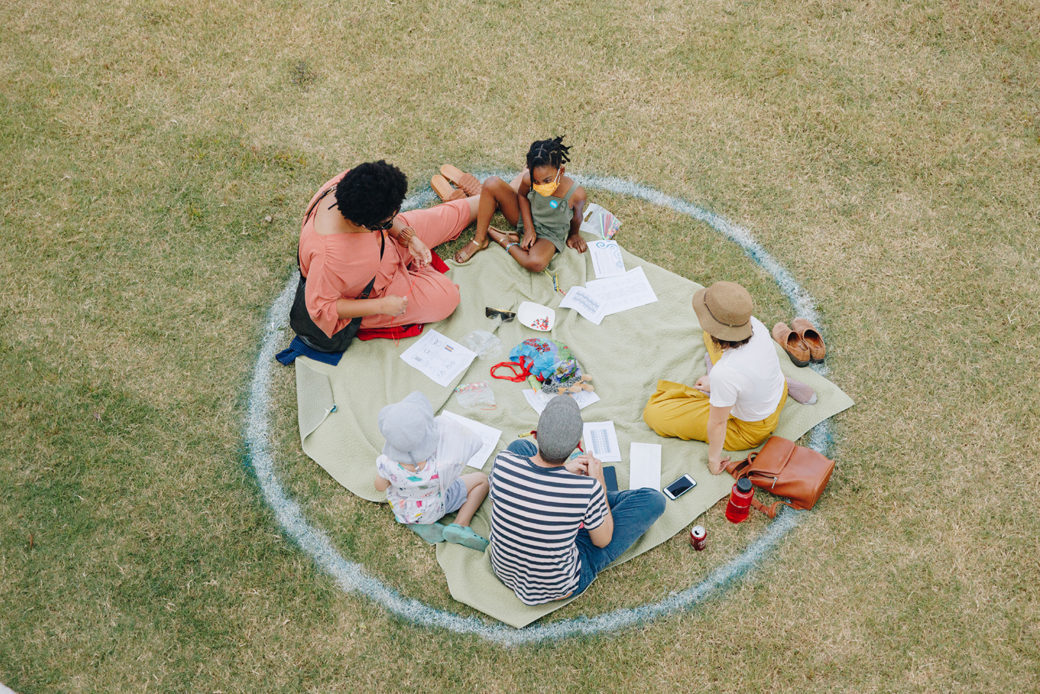 Three adults and a child sit inside a marked circle on a grassy field