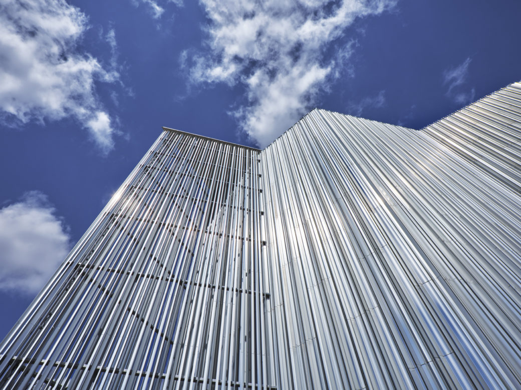 A portion of the outside corner of a building, set against a blue sky with white clouds