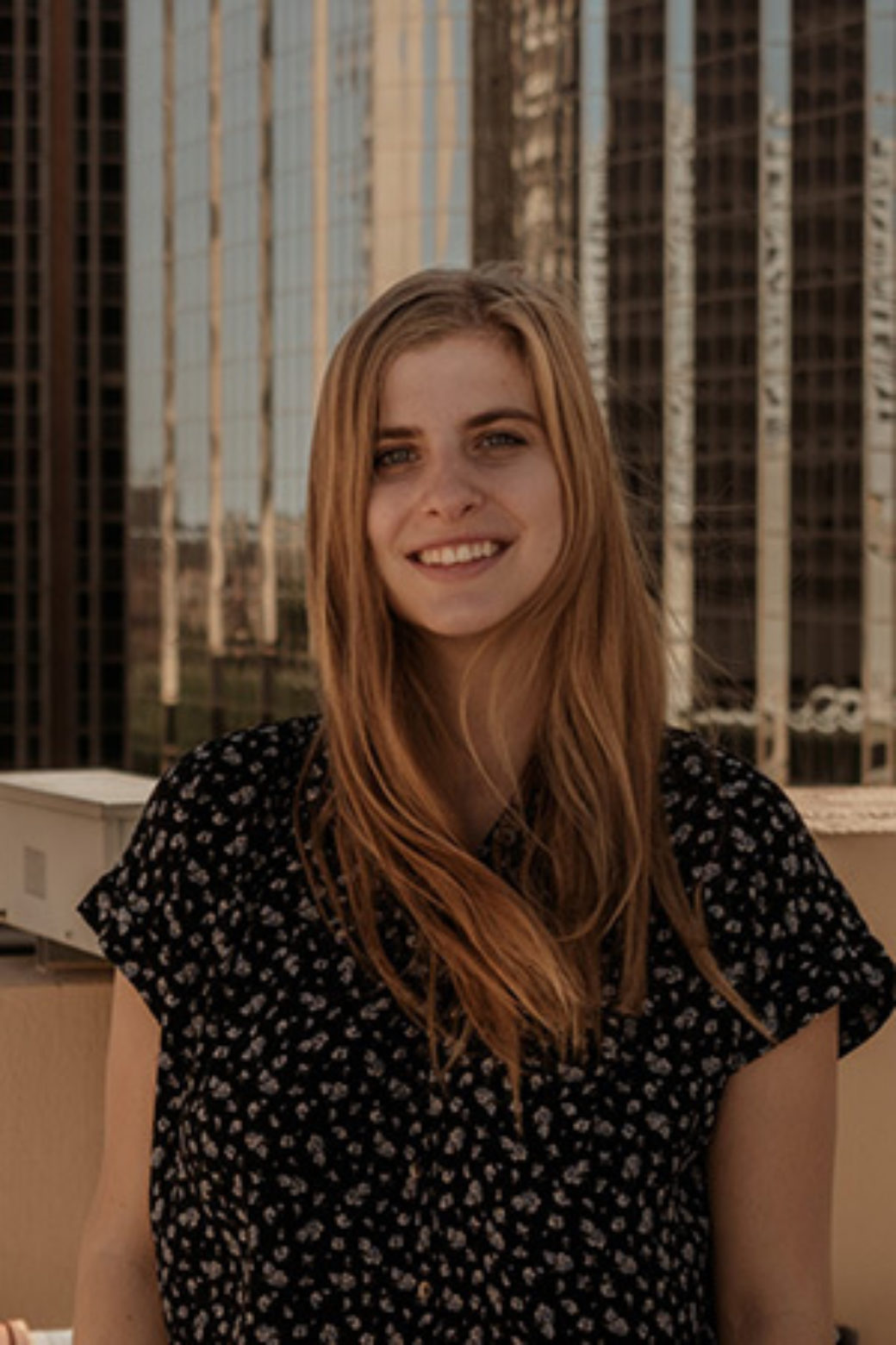 Woman with long strawberry blonde hair smiles at the camera against a city landscape