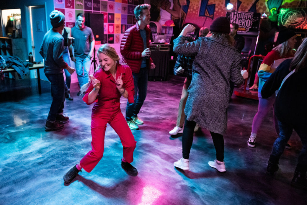 A person in a red jumpsuit dances at a party with multicolored lights