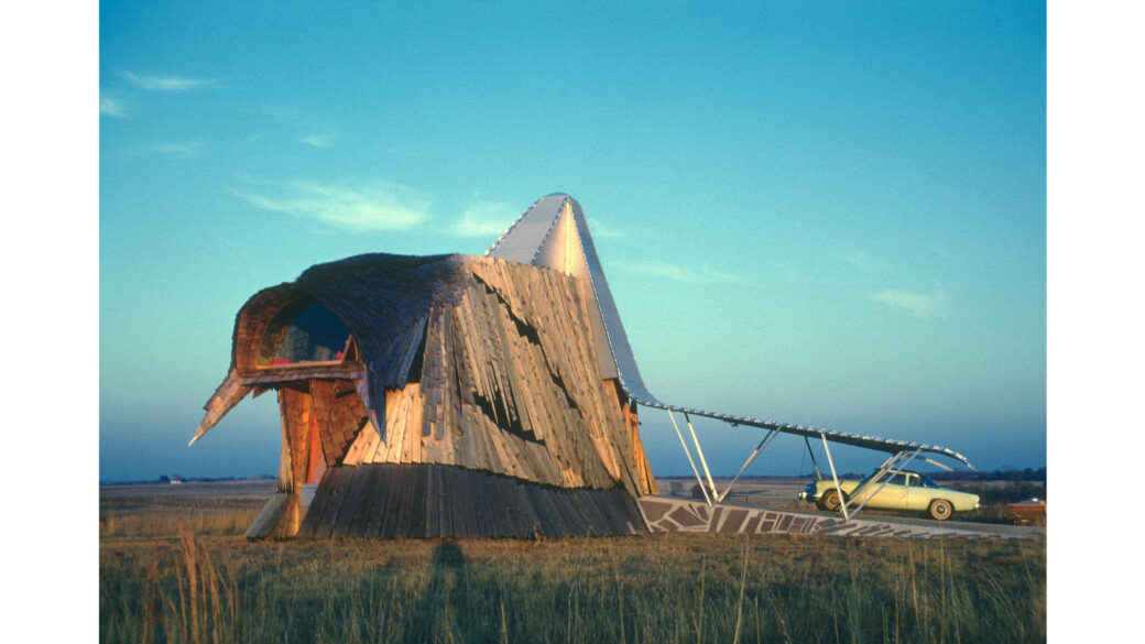A building with a beak-like shape protruding from a triangular frame on a prairie