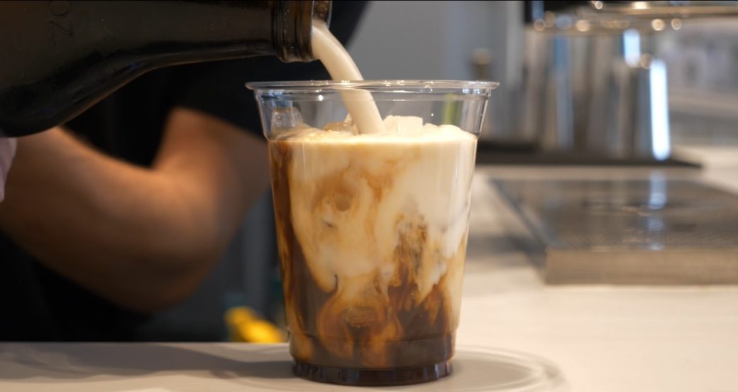 A close-up shot of milk being poured over iced coffee
