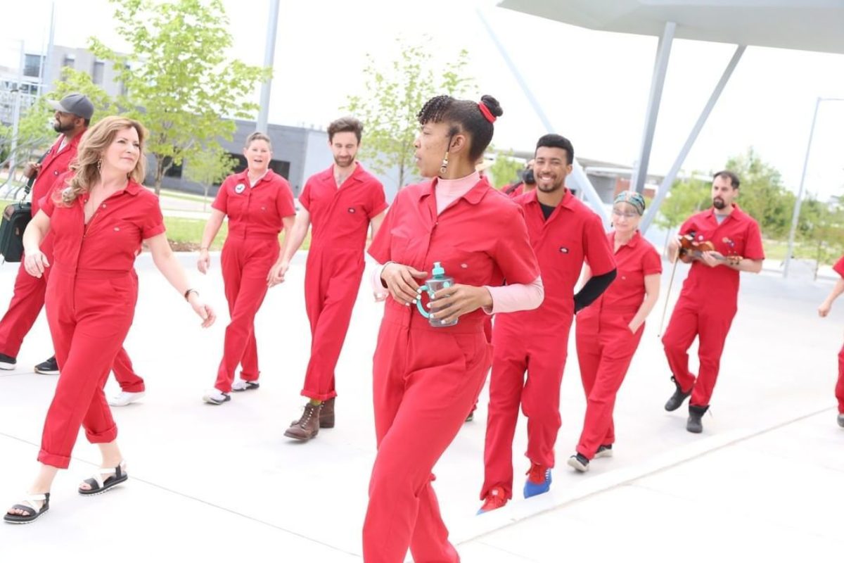 A group of people wearing red jumpsuits walk across a paved surface.