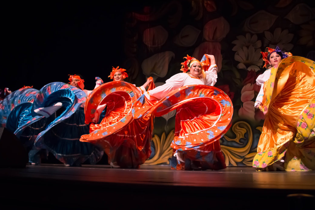 Five dancers in long colorful dresses dance and twirl on stage
