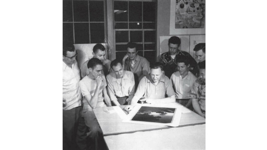 Black and white image of people gathered around a table with large images laid on it