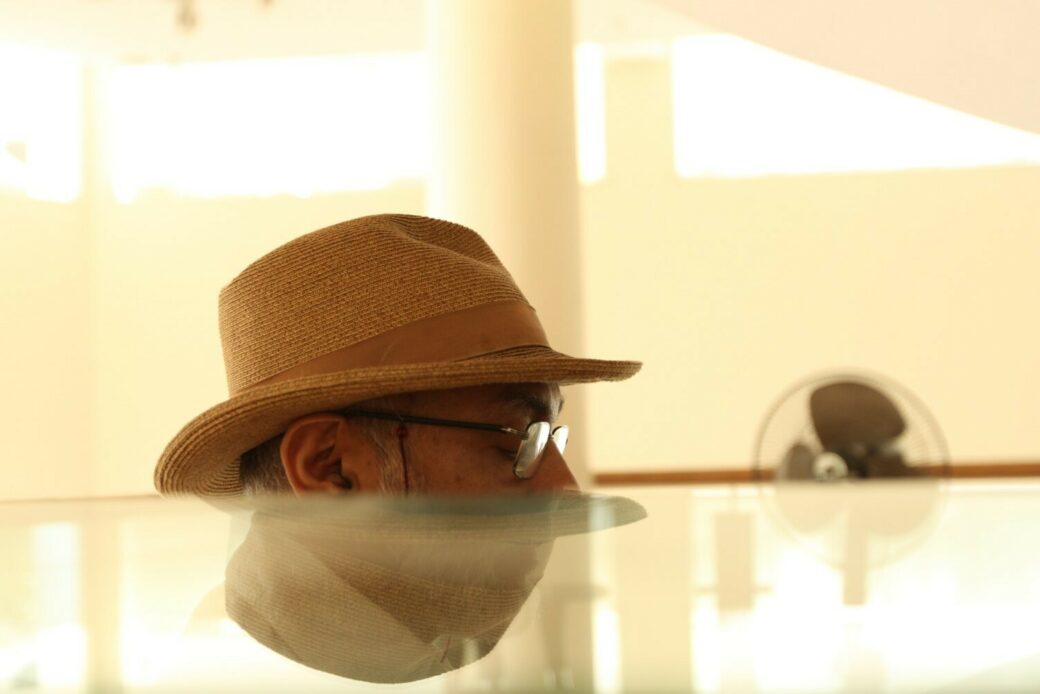 The top half of a man's head wearing a hat and glasses is visible over a reflective surface