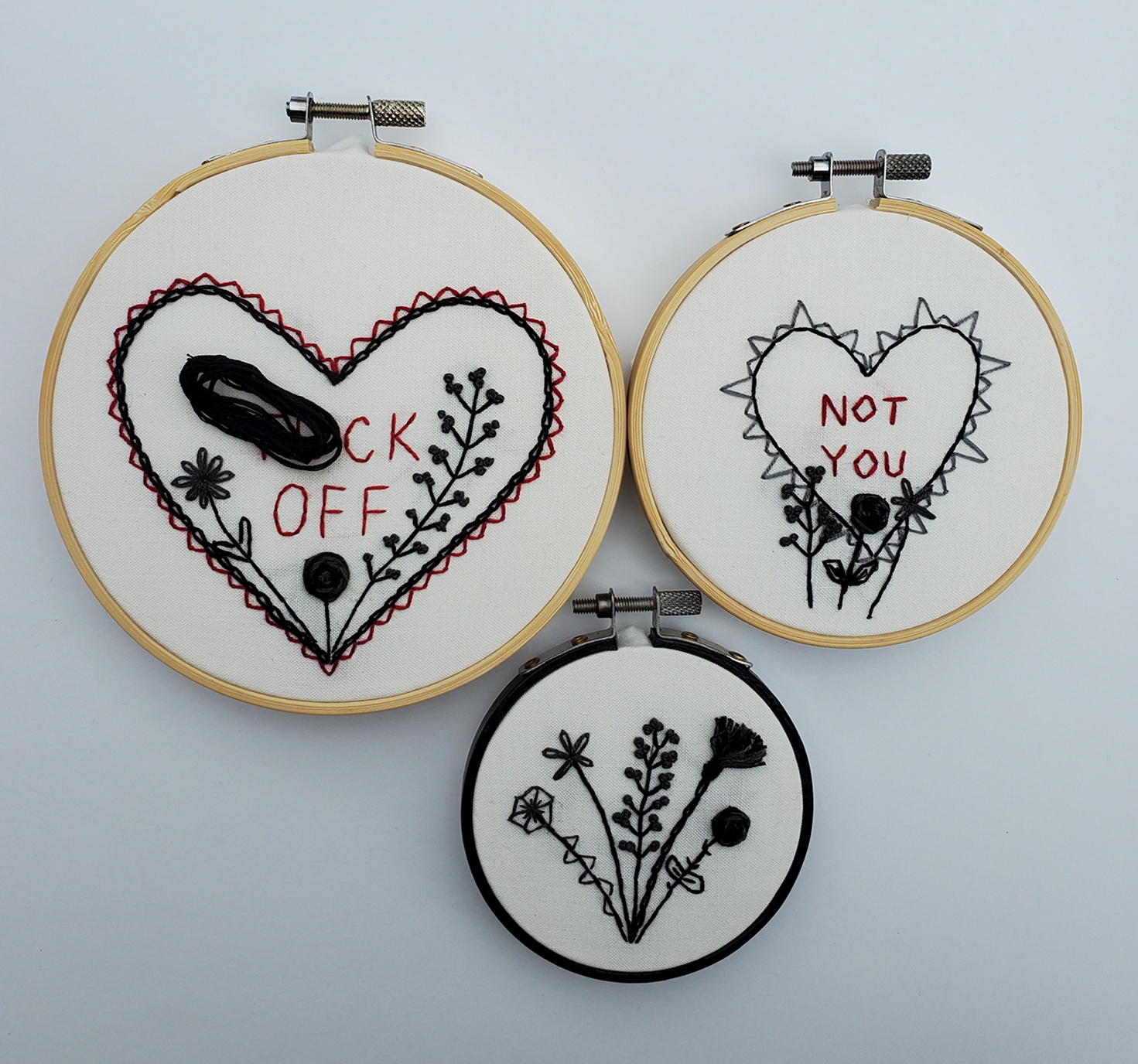 Image of three needlework hoops with hearts, fauna, "#*ck Off" and "Not You" embroidered on them.