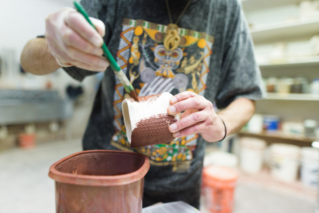 Image of a figure painting brown glaze onto a hand built ceramic cup.