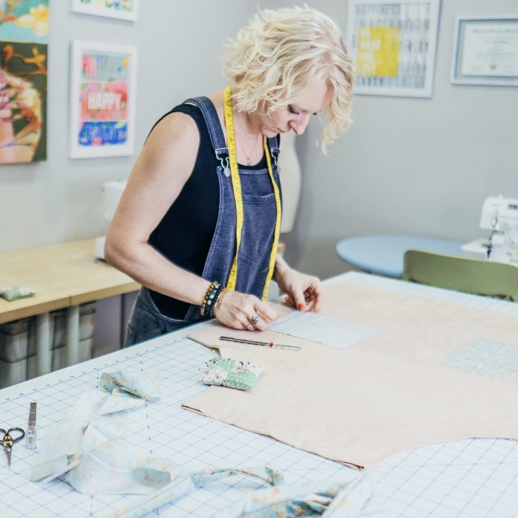 A person stands at a cutting table placing pattern pieces on fabric
