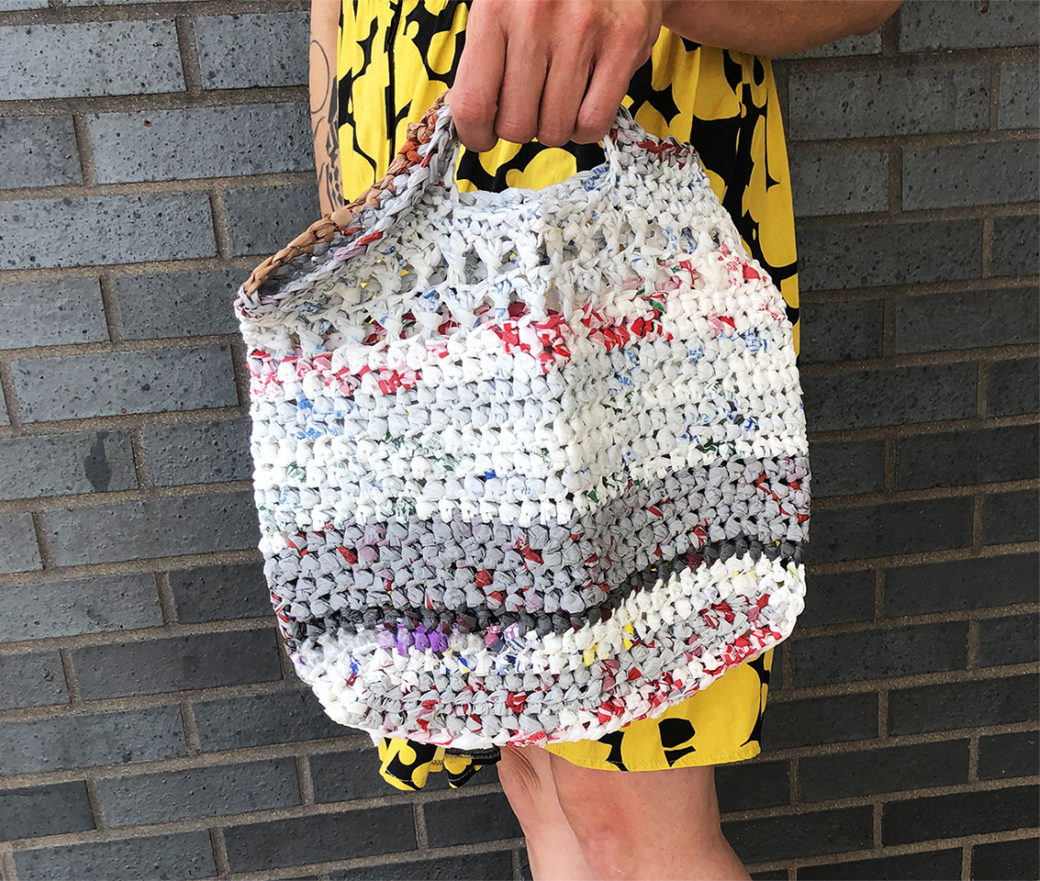 A crocheted bag held by a person in a black and yellow dress