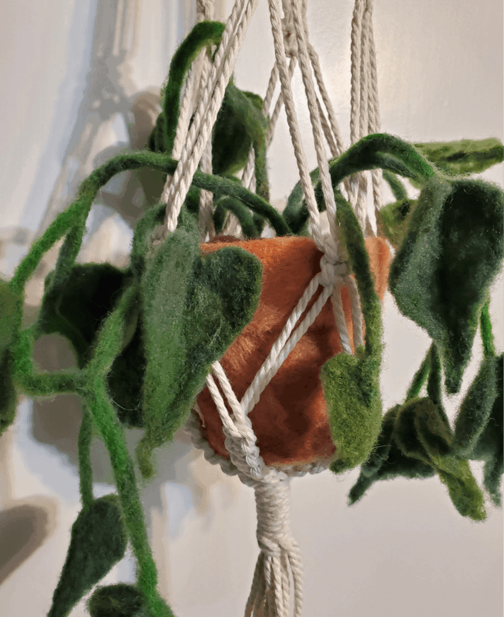 A felted plant in a terracotta pot displayed in a macrame hanger