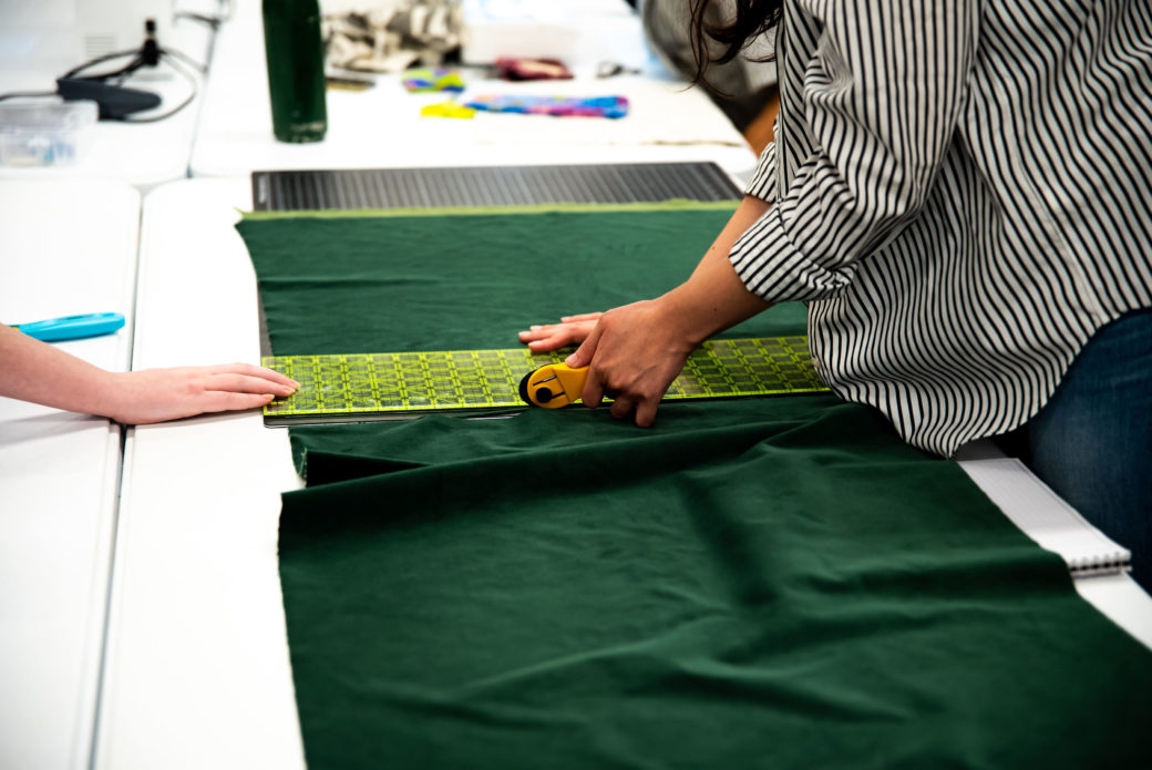 close up image of hands cutting a piece of green fabric