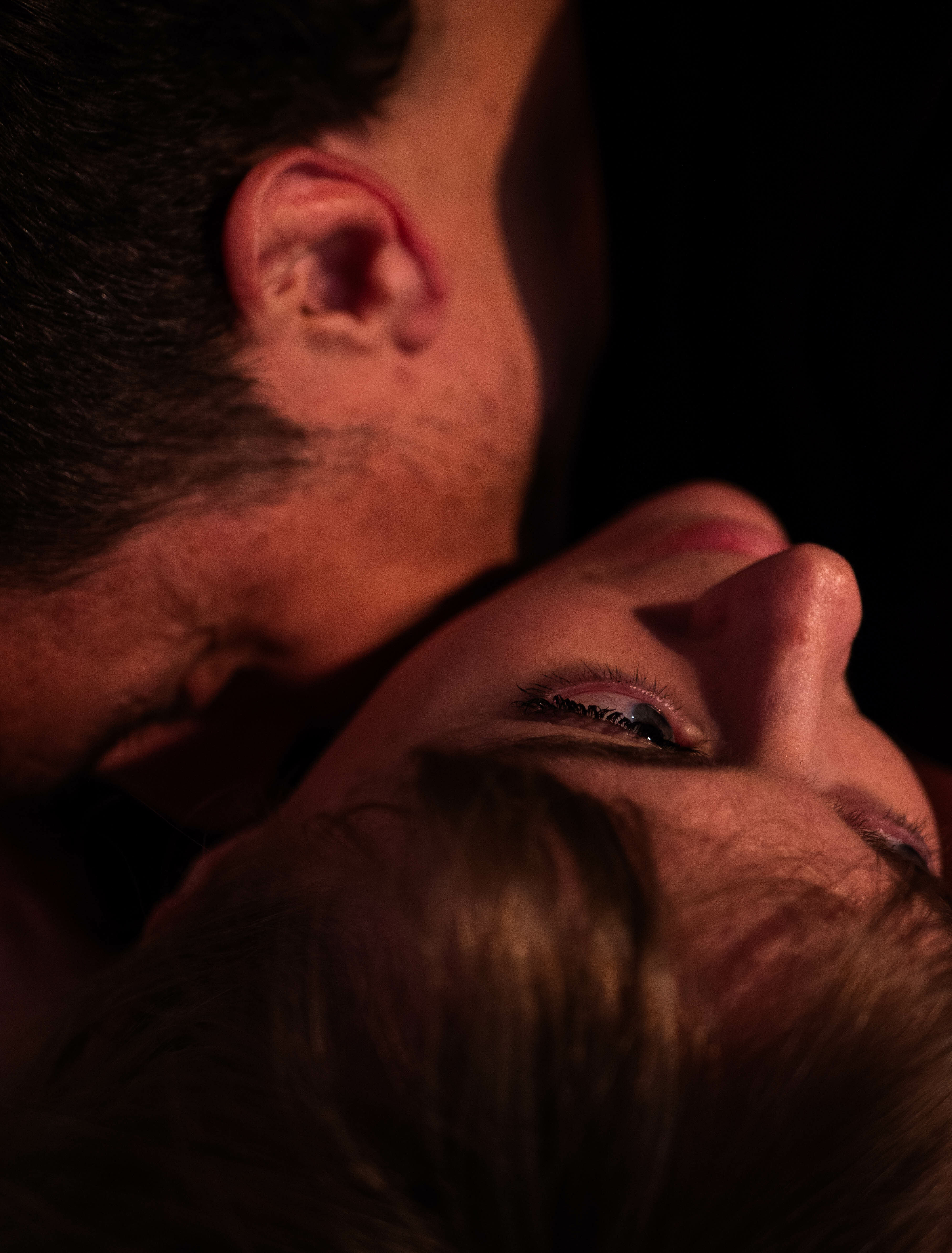 A close up shot of two people. One person's head is rolled back, while the other's face is tucked into the neck of their partner, only showing the side of their head and ear.