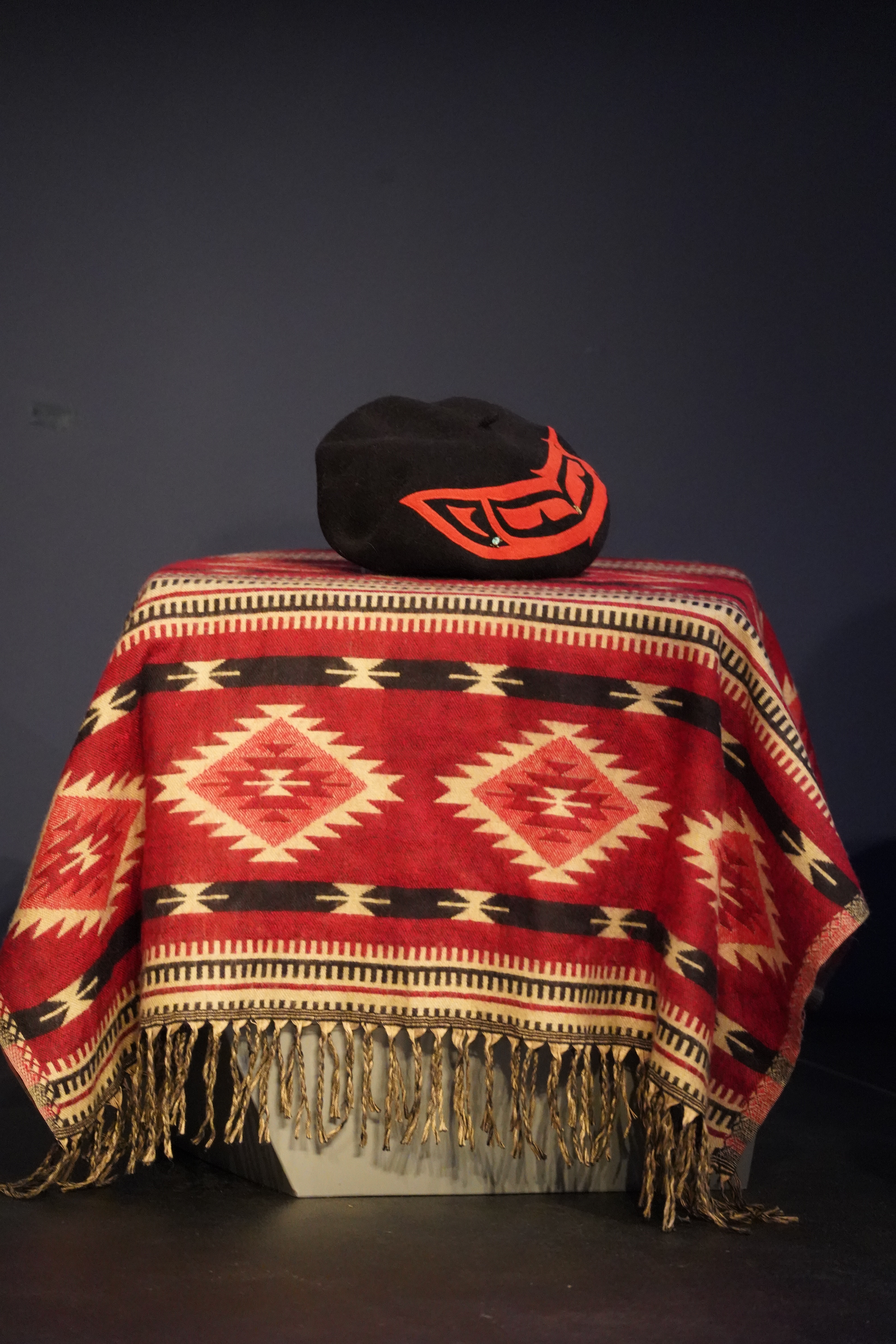 A black beret with a red design sits atop a red blanket with black and cream designs and patterns.