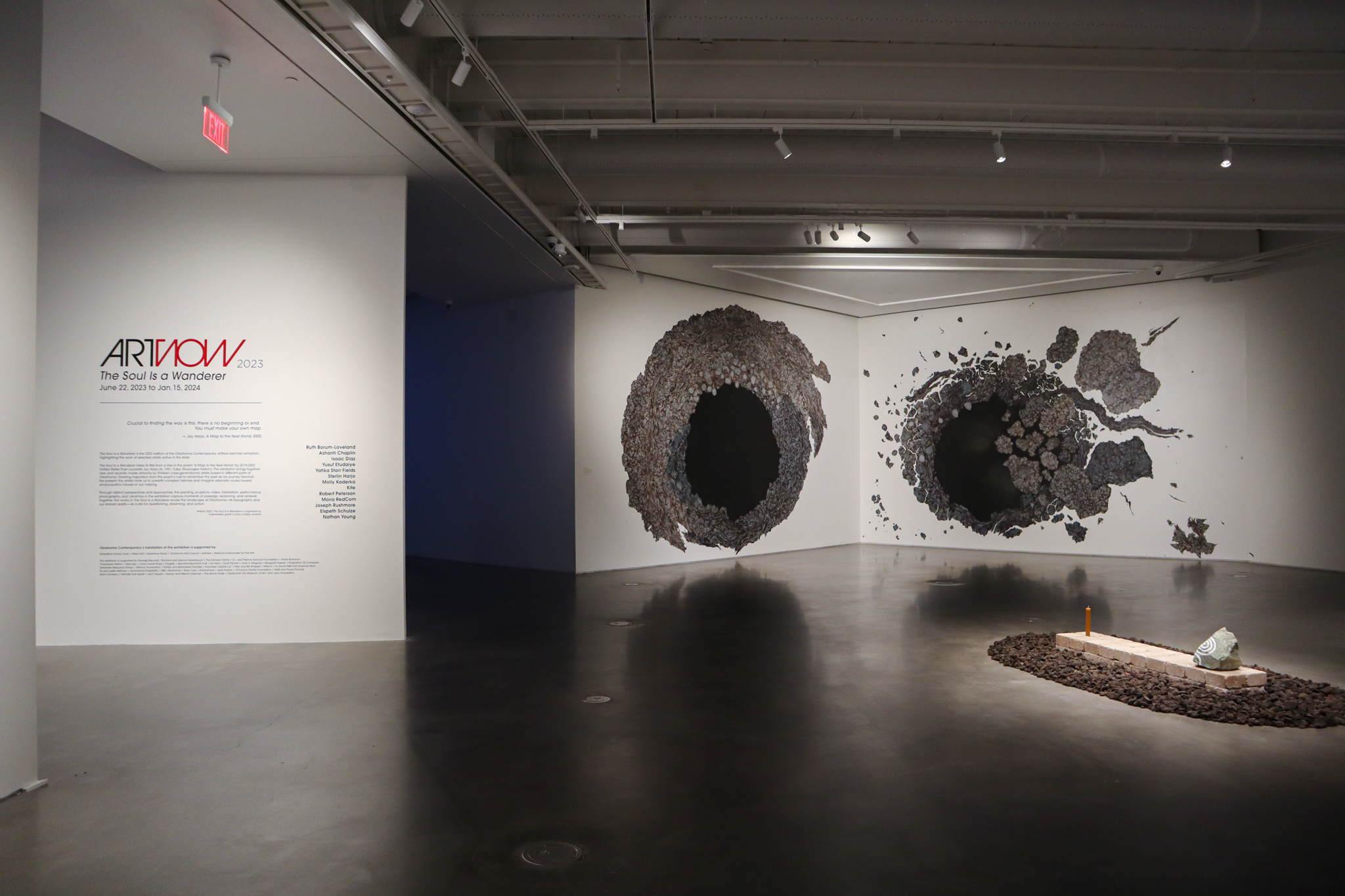 An art gallery with white walls. On the left is the title wall reading, ARTNOW 2023 THE SOUL IS A WANDERER, with text underneath. To the right are large works on adjacent walls, with marbled spheres and large black centers in the middle.