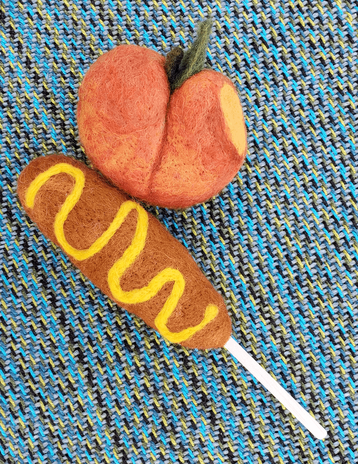 A felted corndog with mustard next to a felted peach