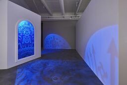An art installation featuring a human figure and various shapes casts blue light across an empty gallery space