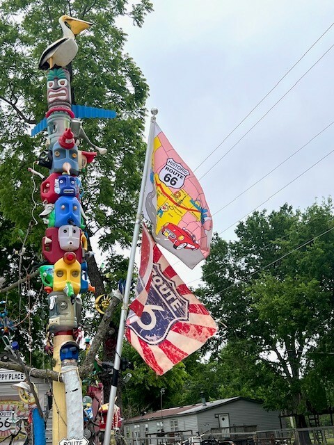 A totem pole topped with a pelican next to two Route 66 flags