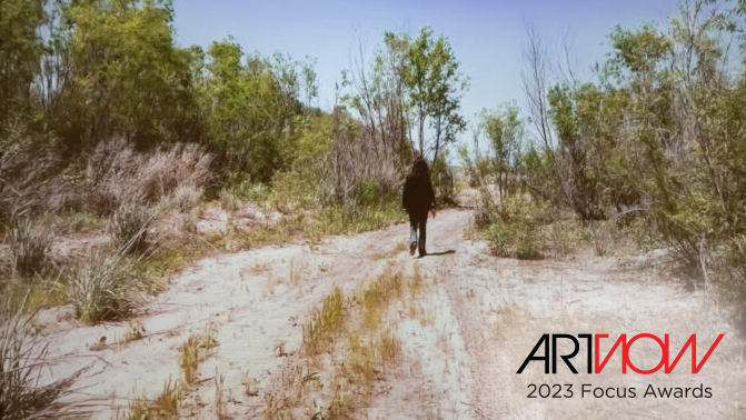 A woman in black walks down a dirt path away from the camera. "ArtNow 2023 Focus Awards" is written in the lower right corner.