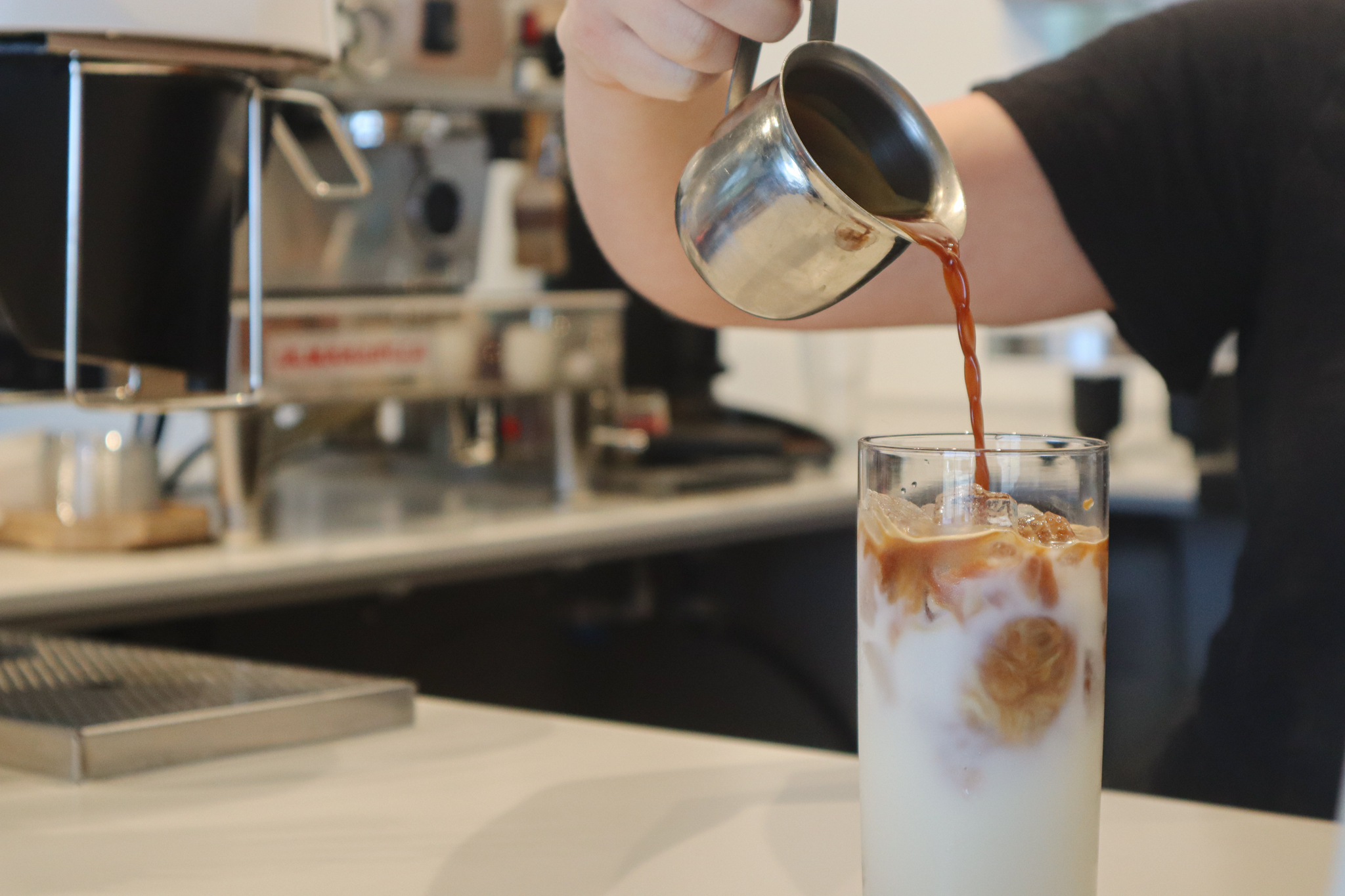 A hand pours coffee into a glass of iced milk