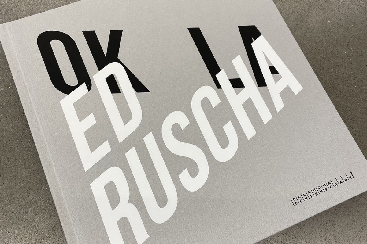 A square, gray book reads "ED RUSCHA OK LA" in black and white text