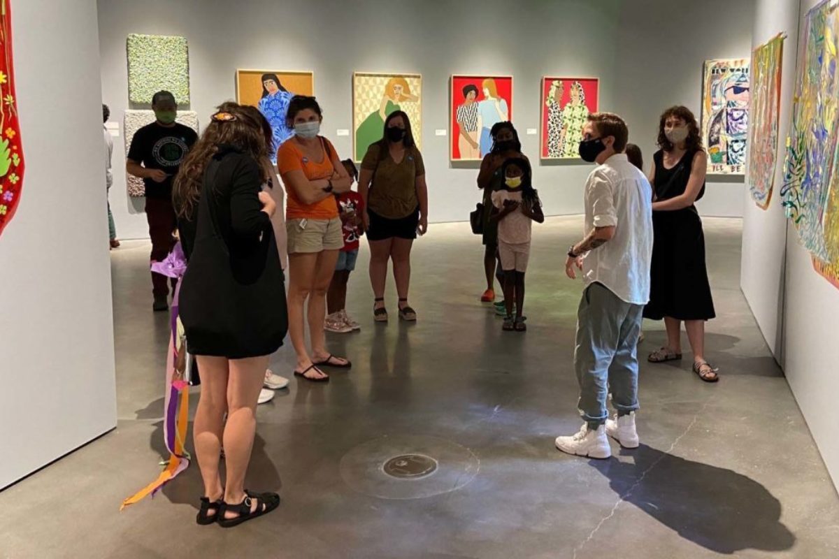 A group of people stand together in a gray-walled gallery featuring numerous artworks